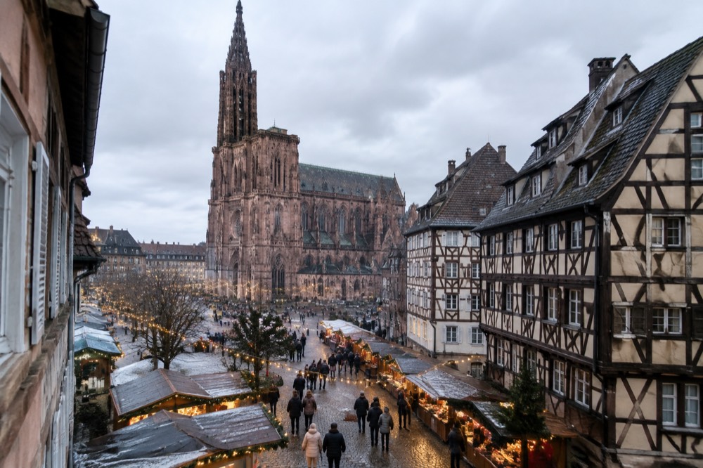 Festive market stalls in Strasbourg with lights strung above the street and shoppers in winter coats