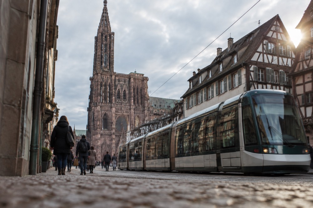 A tram passing through a Strasbourg street with shoppers walking on the pavement