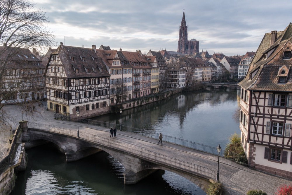 Wide level bridge over the Ill with half-timbered facades along the bank