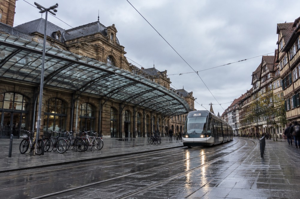 A tram gliding along a city street lined with timber-framed buildings in daylight