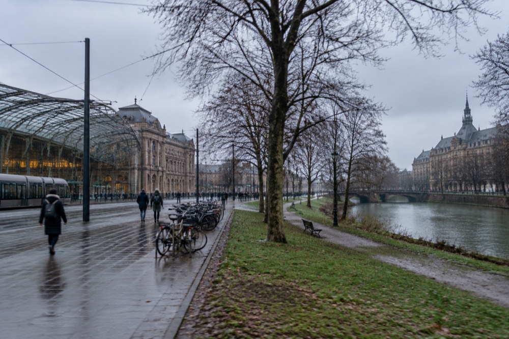 A park beside a river with bare winter trees and a historic building in the background