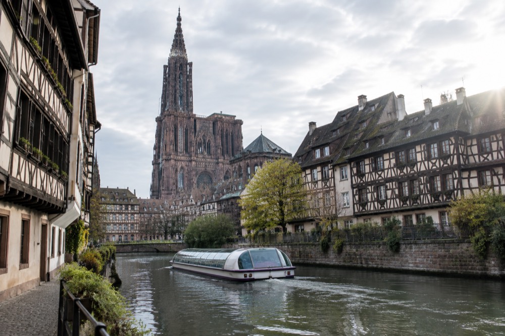 A glass-roofed sightseeing boat passing half-timbered houses along a narrow channel of the River Ill in Strasbourg