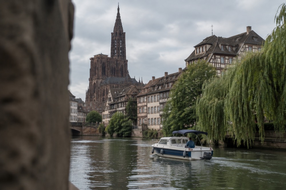 A small private boat with a skipper cruising past willow trees along a quiet stretch of the River Ill near Strasbourg