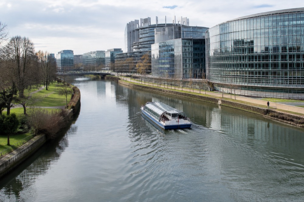 A sightseeing boat passing the modern buildings of the European Quarter reflected in the River Ill in Strasbourg