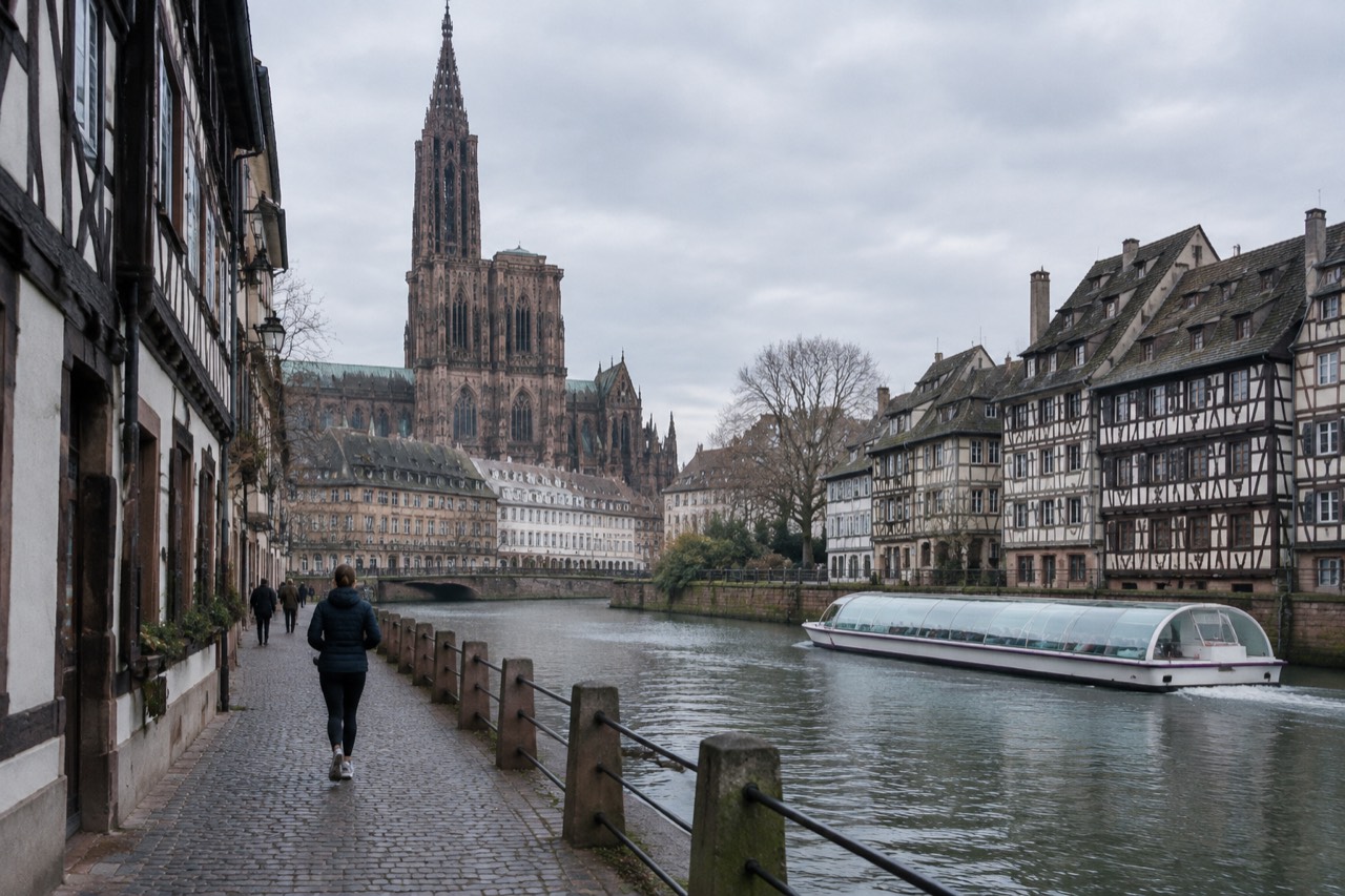 A glass-roofed sightseeing boat cruising the River Ill past half-timbered houses along the Strasbourg waterfront