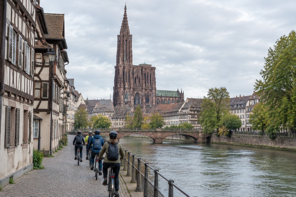 A small group of cyclists following a guide along a riverside lane in Strasbourg