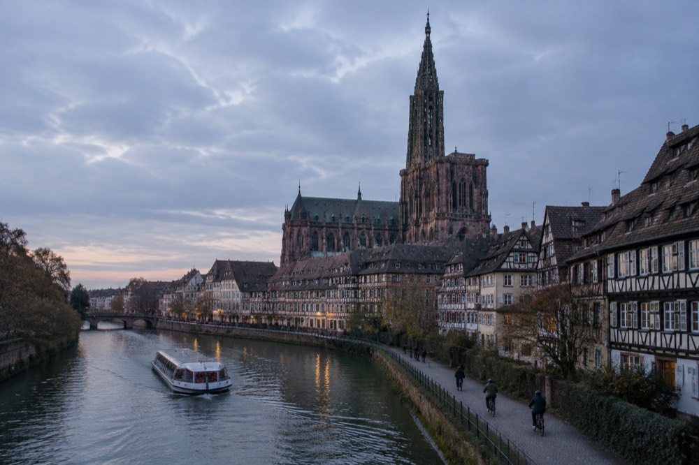 A river boat passing cyclists on the towpath beside the Ill in Strasbourg