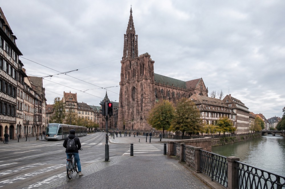 A cyclist waiting at a tram crossing in a wide boulevard in central Strasbourg