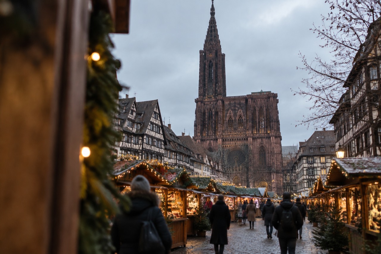 Wooden Christmas chalets with glowing garlands lining a Strasbourg square at dusk
