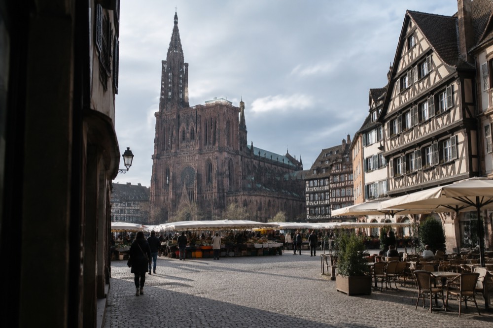 Market stalls and cafe terraces on a stone square in Strasbourg in sunshine