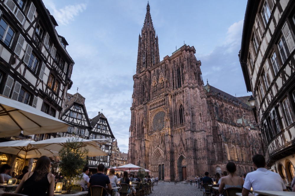 Diners at outdoor tables on a Strasbourg square in summer with the cathedral behind