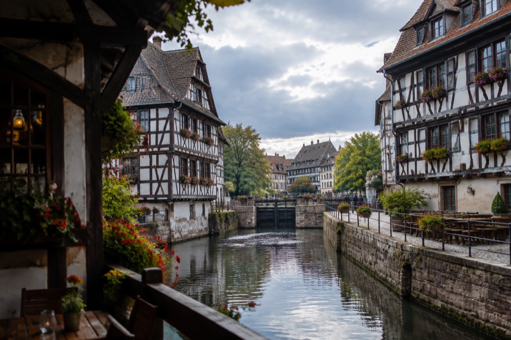 A half-timbered winstub facade with a hand-written menu board on a narrow Strasbourg street at dusk