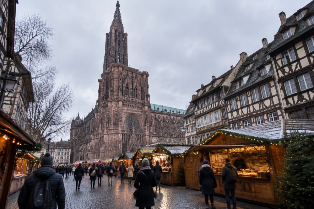 Wooden Christmas market chalets with lights and food stalls around Strasbourg cathedral at dusk