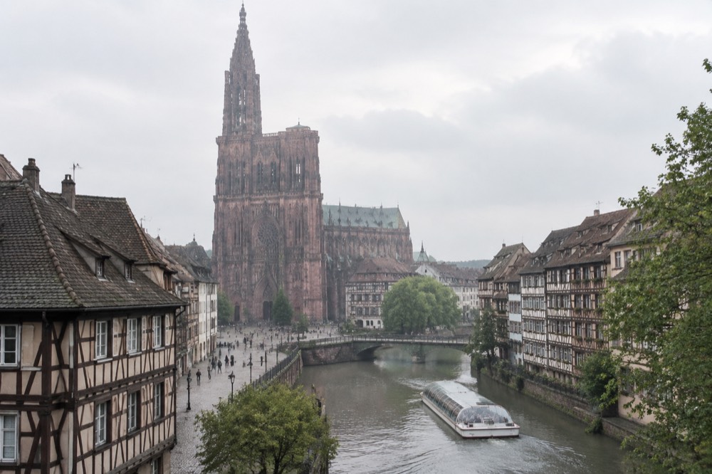 A canal boat passing half-timbered houses along the River Ill in Strasbourg on a bright afternoon