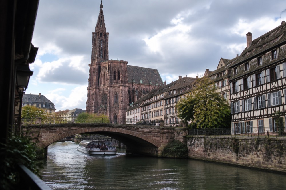 A sightseeing boat passing under a stone bridge on the Ill river in Strasbourg
