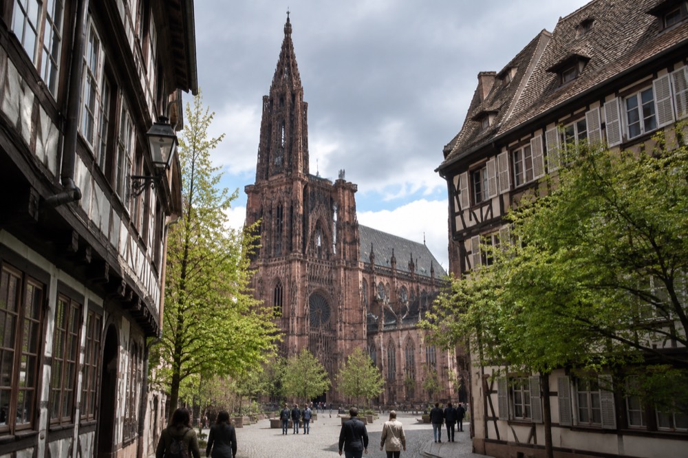 The single spire of Strasbourg Cathedral seen from a narrow old street in spring light