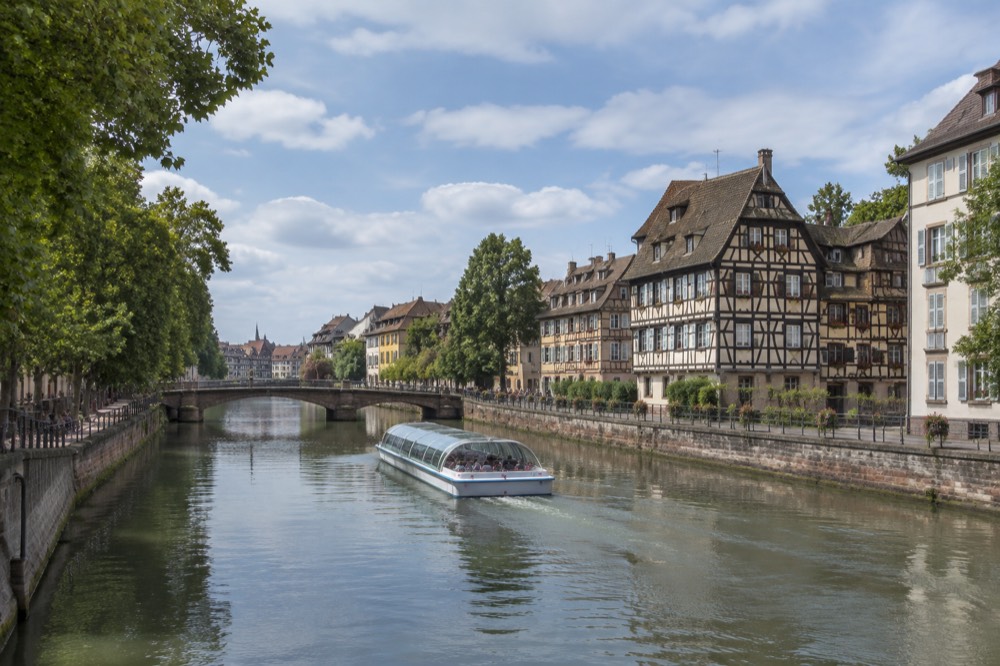 A river boat passing half-timbered buildings along the Ill in summer