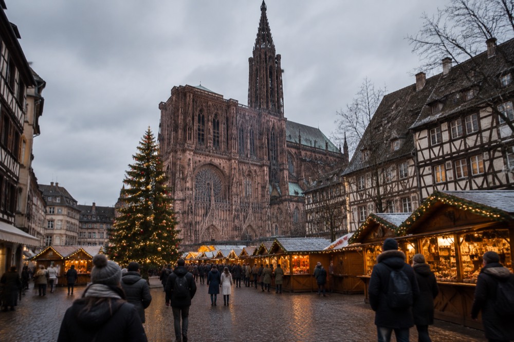 A Christmas market square in Strasbourg at dusk with a large decorated tree and wooden chalets