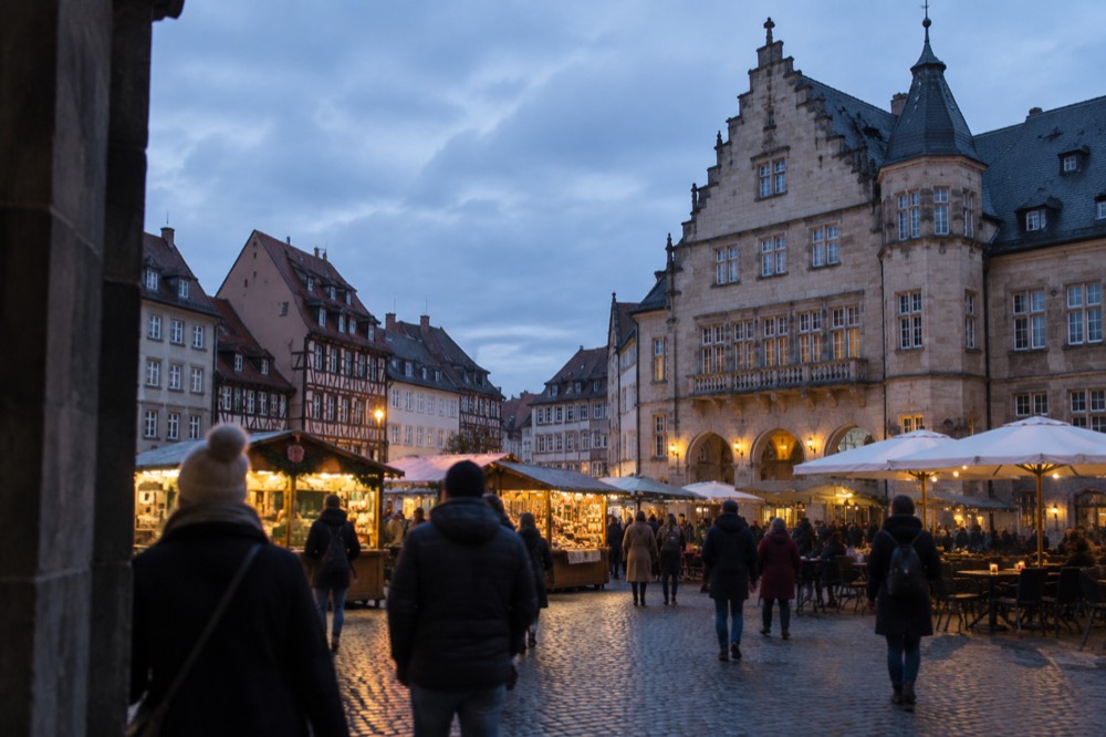Market visitors in warm coats walking past illuminated stalls on a cold evening