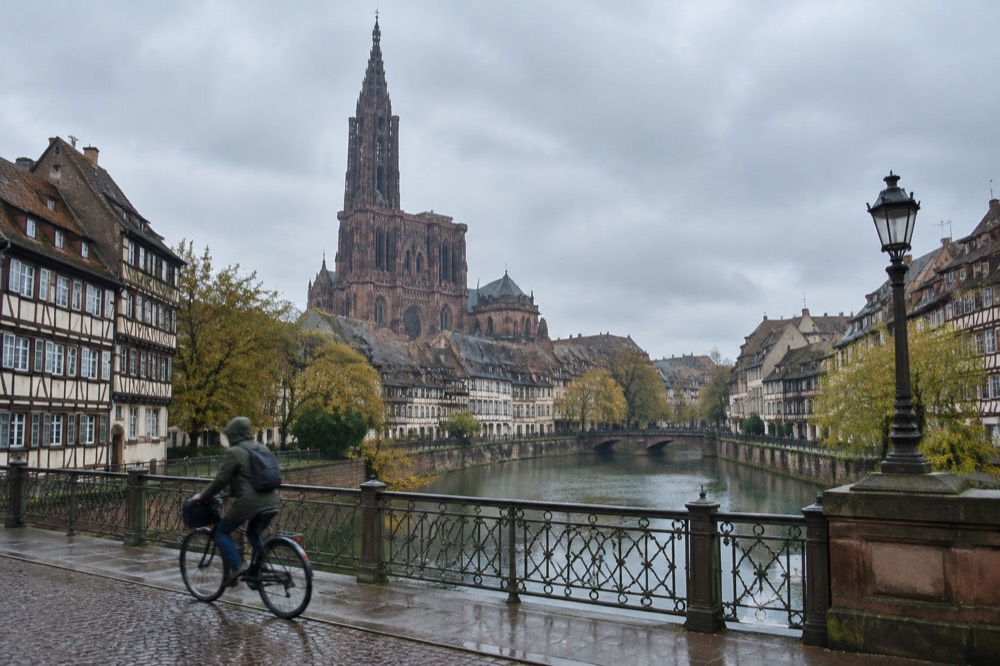 A cyclist crossing a Strasbourg bridge over the Ill with the old town behind