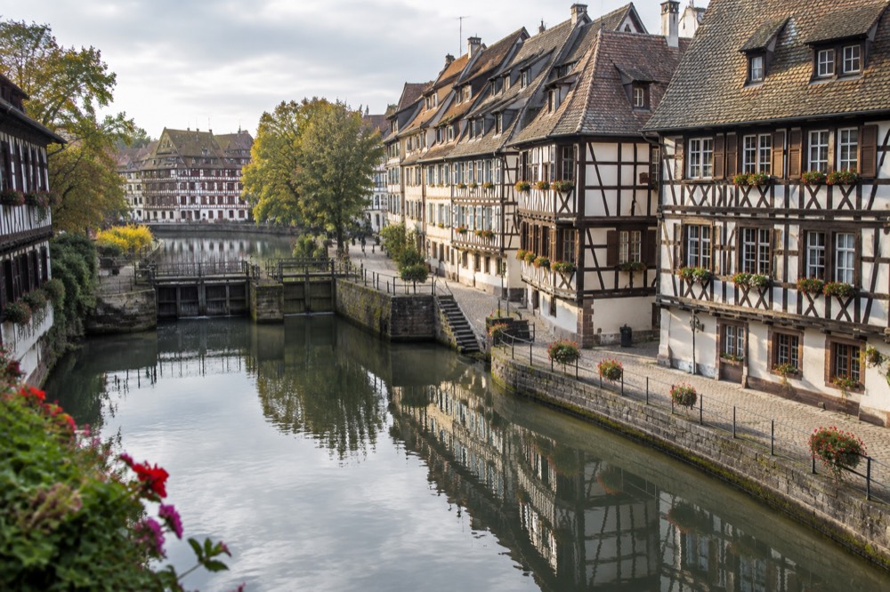 Canal-side half-timbered buildings in Petite France reflected in still water on a bright morning