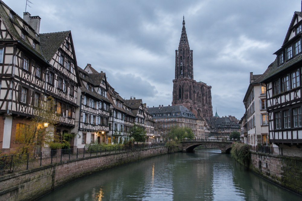 Half-timbered houses along a canal in Strasbourg with the cathedral spire rising above the rooftops