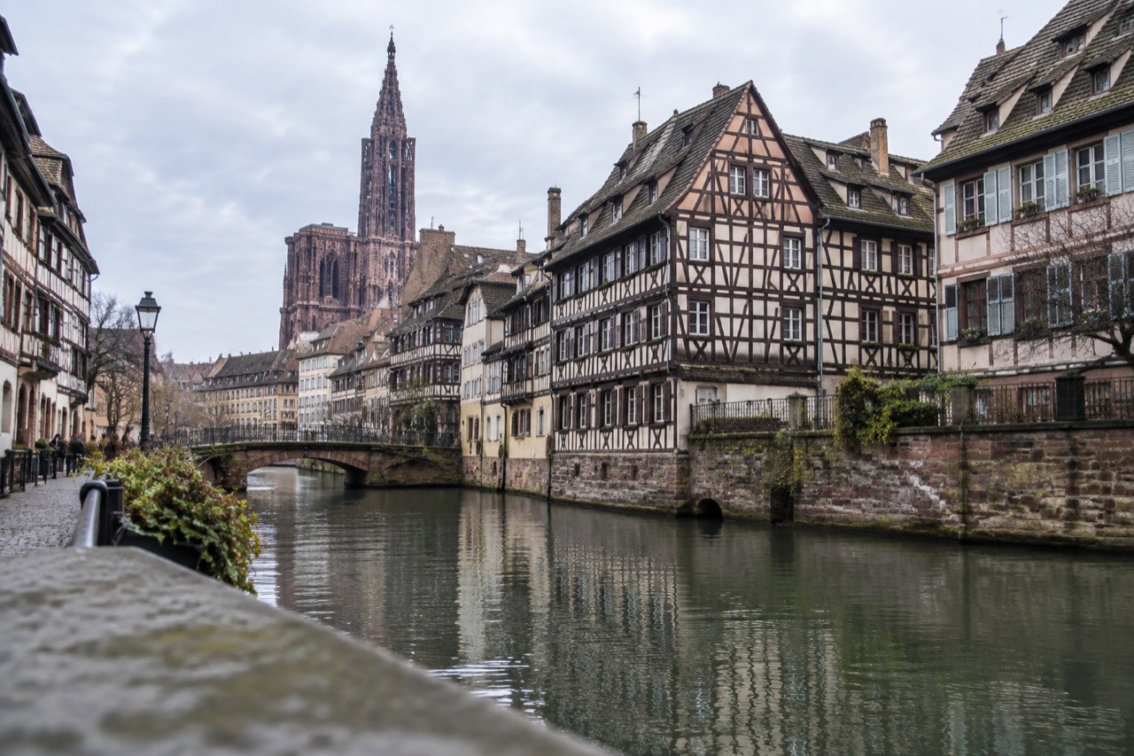 Half-timbered houses along a canal in Strasbourg with the cathedral spire rising above the rooftops