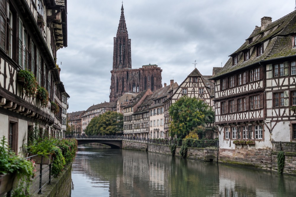 Half-timbered houses along a canal in Strasbourg with the cathedral spire rising above the rooftops