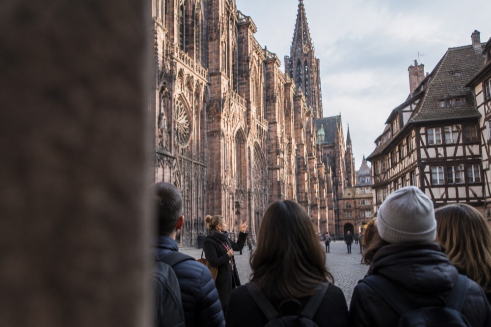 A guide speaking to a small group on a cobbled square in front of Strasbourg Cathedral