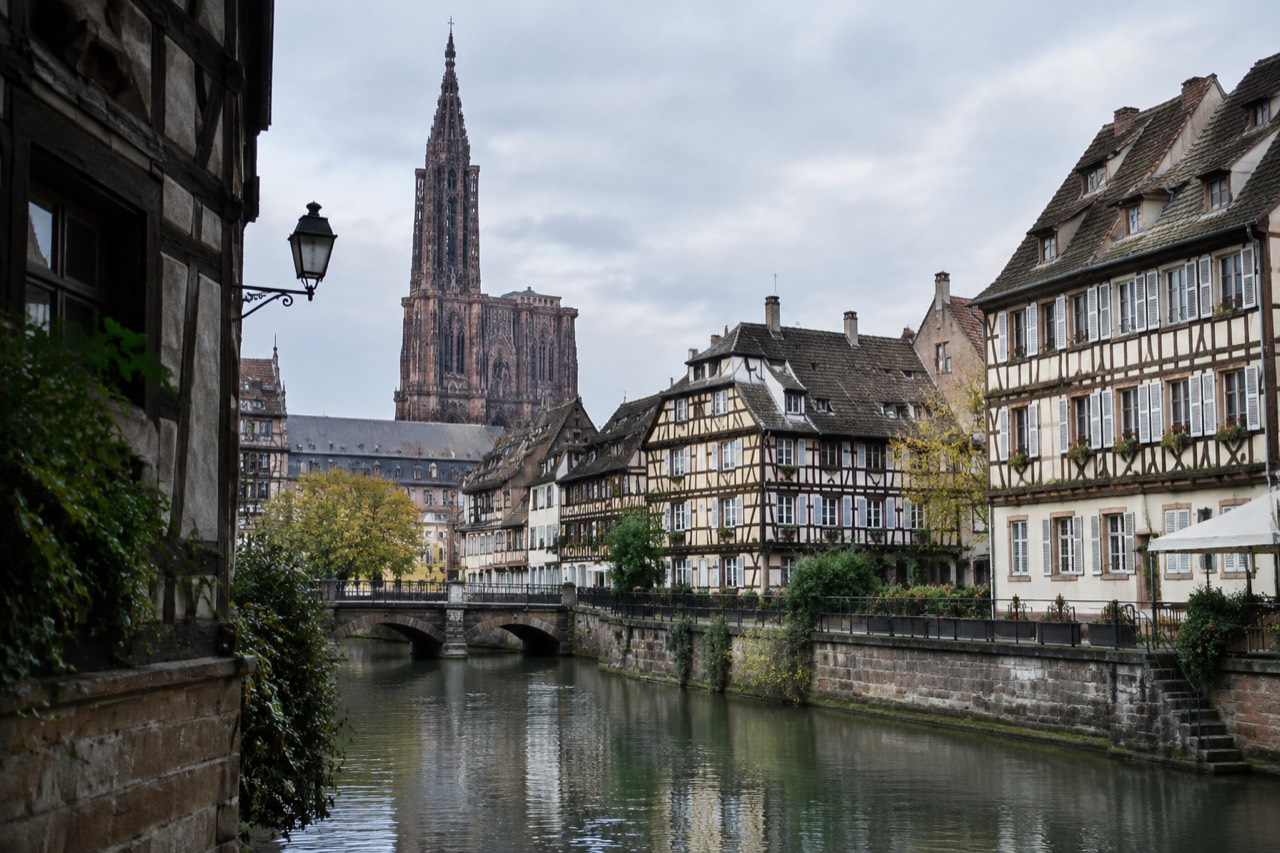 Half-timbered houses along a canal in Strasbourg with the cathedral spire rising above the rooftops