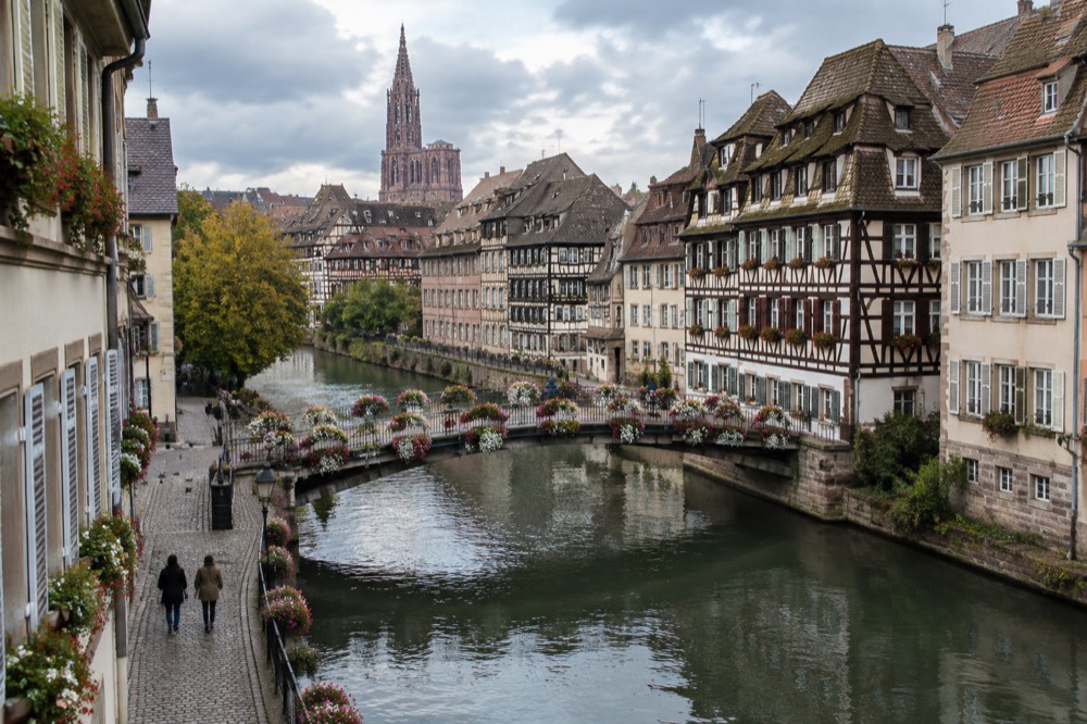 Flower-covered footbridge over the Ill river with half-timbered buildings behind it