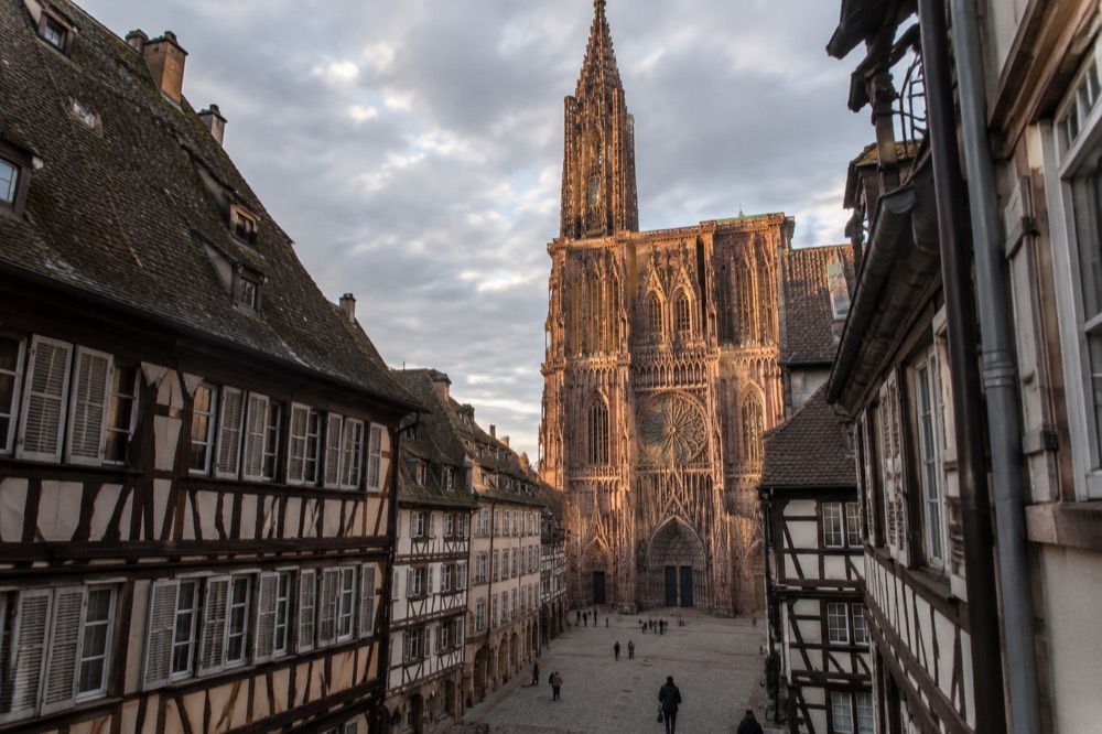 The rose-coloured sandstone facade of Strasbourg Cathedral seen from a narrow square