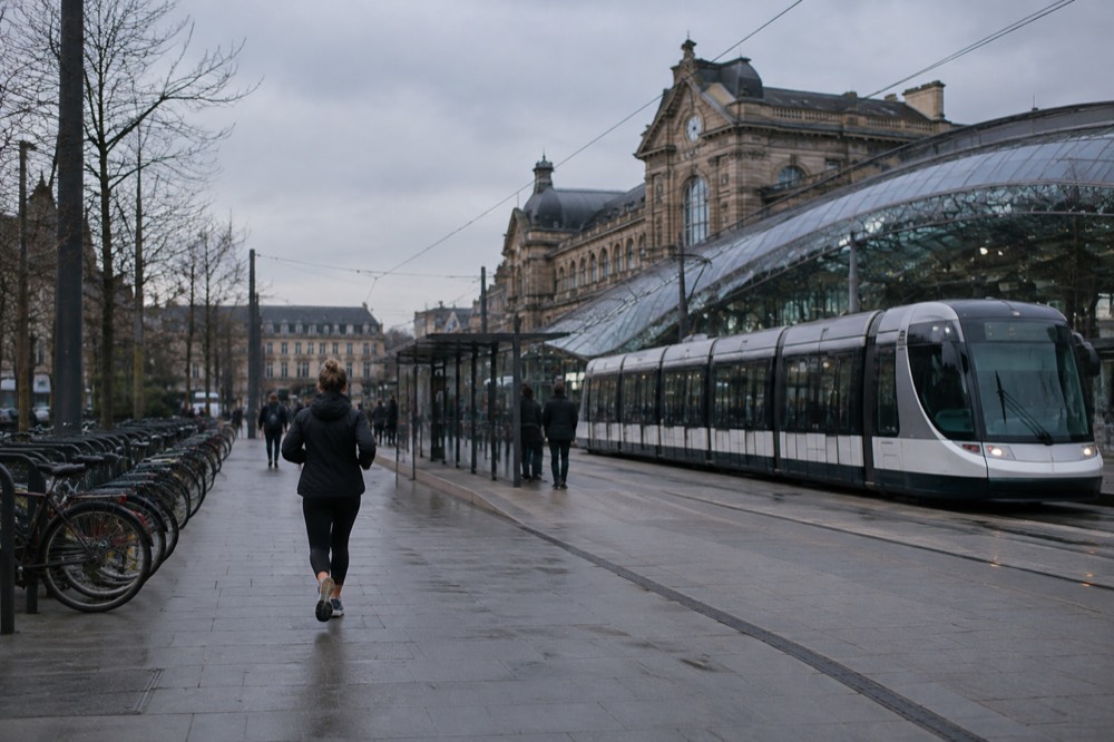 A modern tram passing a stop outside a railway station entrance