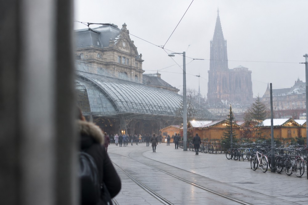 Wooden chalets decorated with lights and garlands in a city square with a gothic cathedral behind