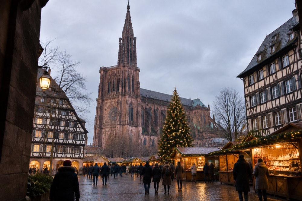 Illuminated Christmas market chalets and a decorated tree in a Strasbourg square at dusk
