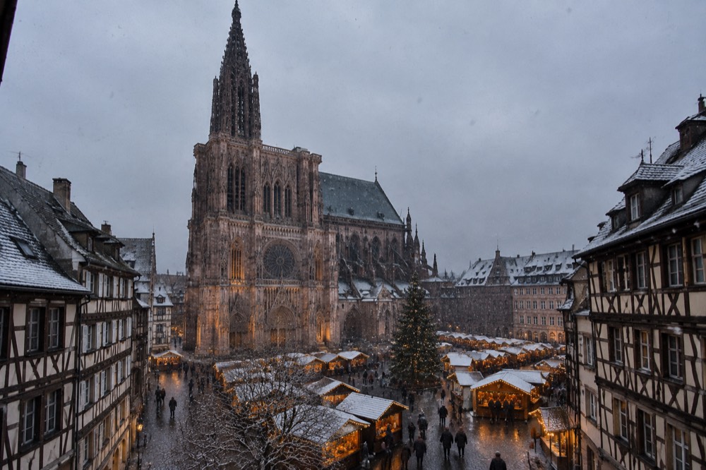 Christmas market chalets and the cathedral under falling snow in the evening