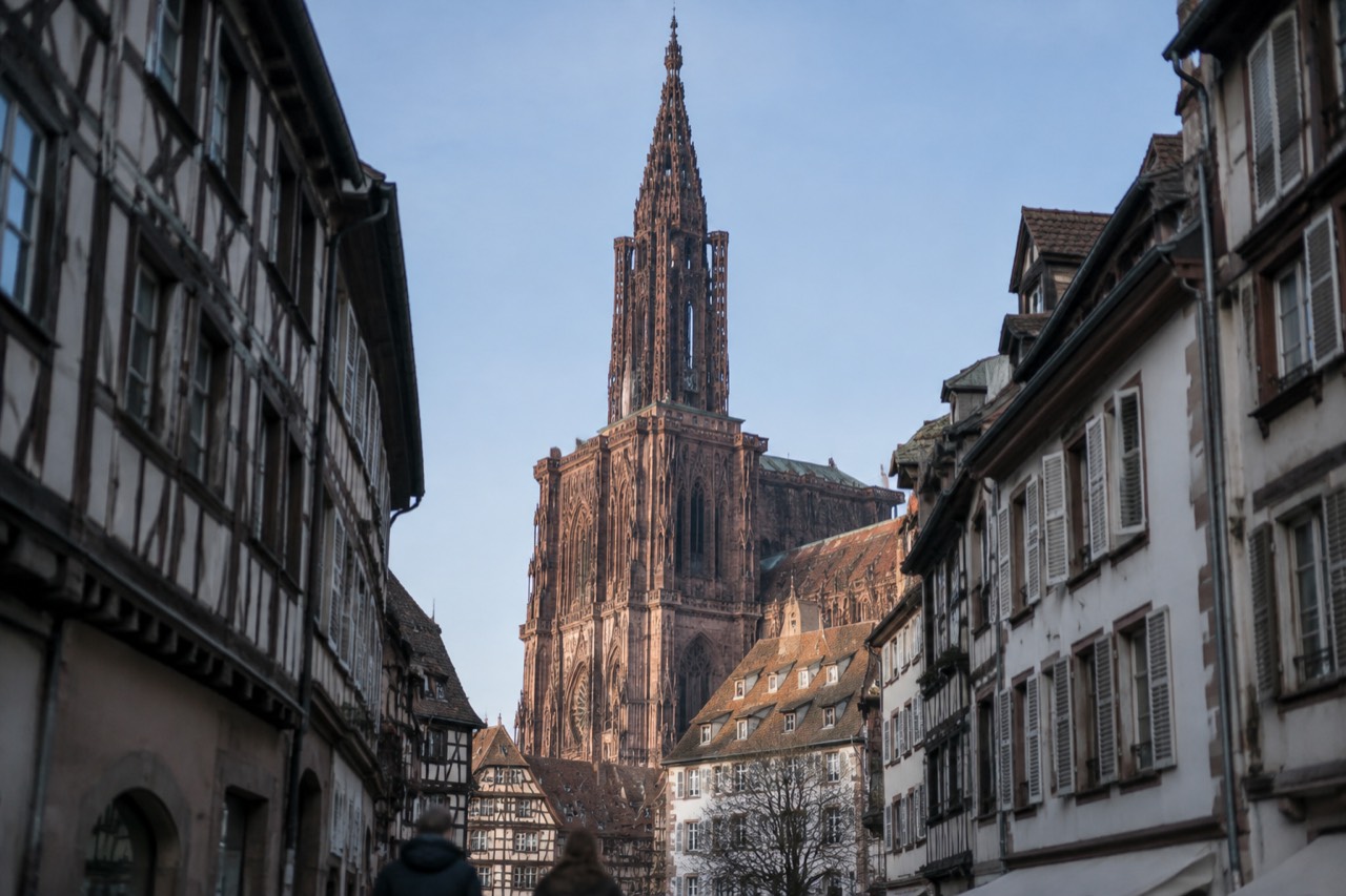 Strasbourg Cathedral's single spire rising above red rooftops under a clear blue sky
