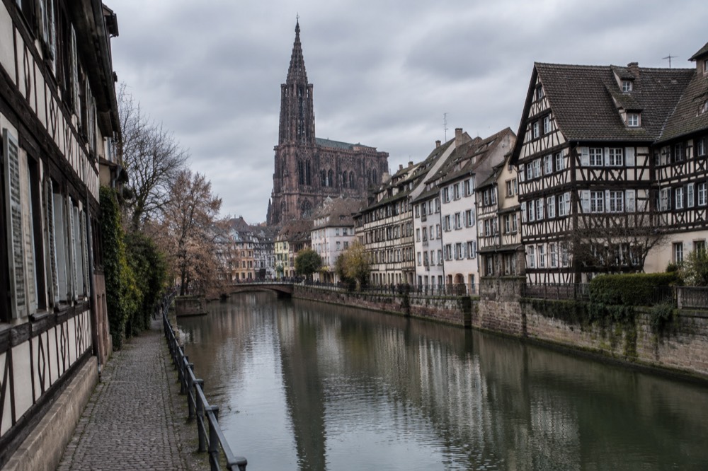 Half-timbered houses along a quiet canal in Strasbourg with the cathedral spire rising over the rooftops