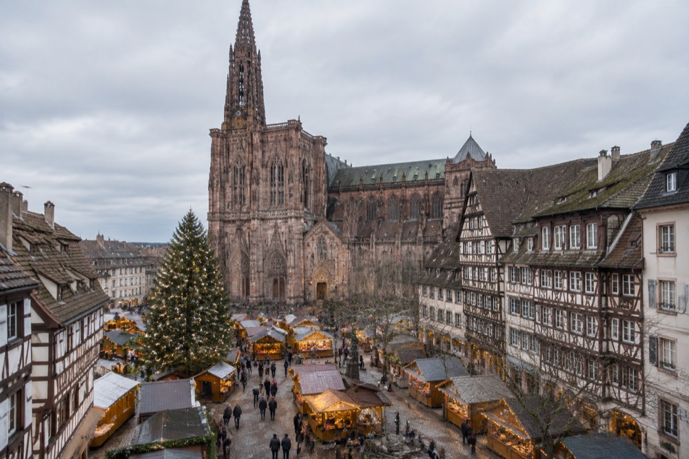 Illuminated Christmas market chalets and a large decorated tree in a historic square in Strasbourg