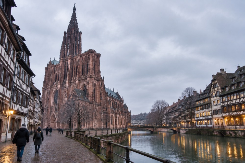 A riverside view of illuminated half-timbered buildings reflected in the Ill at night in Strasbourg