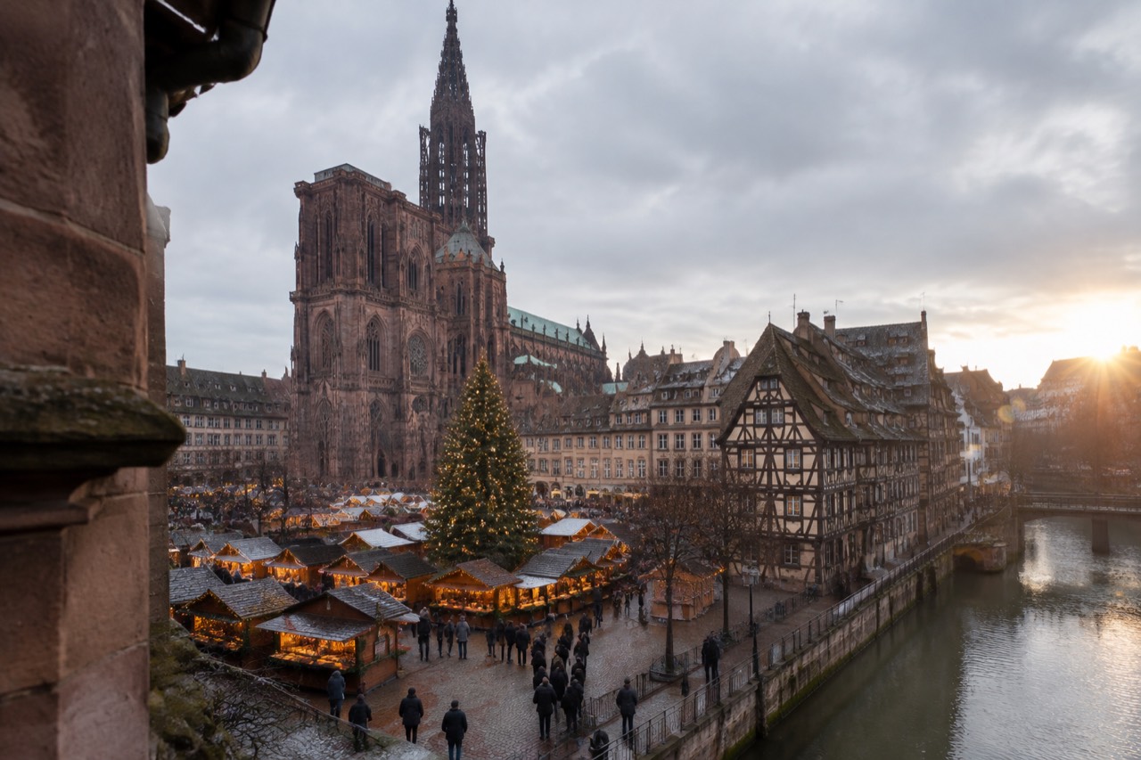 Illuminated Christmas market chalets and a large decorated tree in a historic square in Strasbourg
