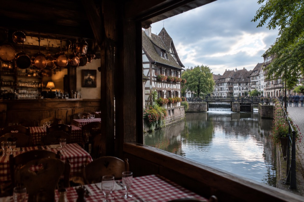A traditional Alsatian tavern interior with wooden beams, checked tablecloths and copper pots hanging above the bar