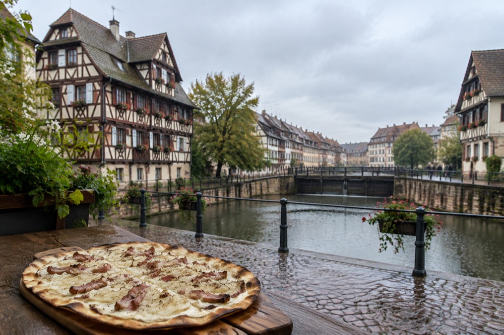 A close view of a tarte flambee on a wooden board, thin and crisp with cream, bacon and onion