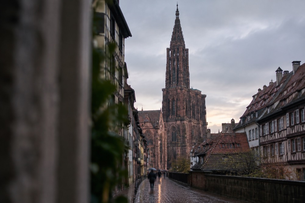 The single spire of Strasbourg Cathedral rising above red rooftops at dusk