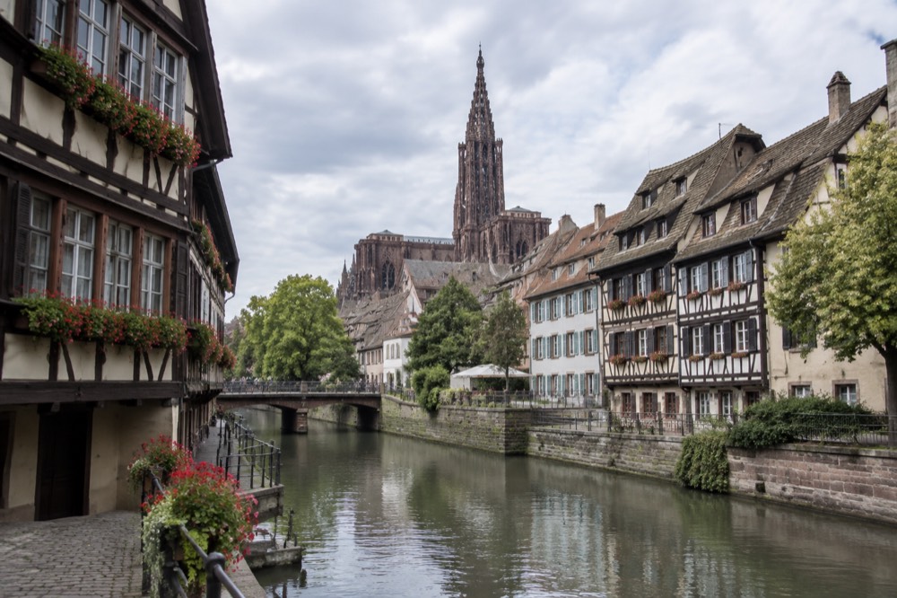 Half-timbered houses along a canal in Strasbourg with the cathedral spire in the distance