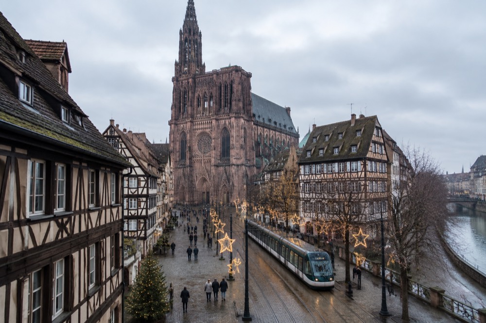 A modern tram passing lit Christmas decorations on a Strasbourg street