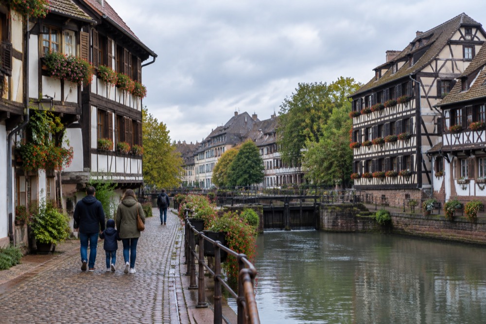 A family walking along a cobbled lane in Petite France with half-timbered houses and the river Ill in the background