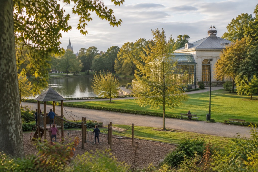 Children playing on a climbing frame in the Parc de l'Orangerie with storks nesting on a rooftop
