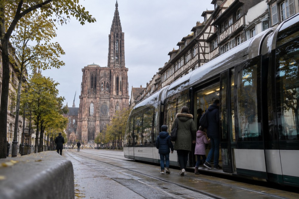 A tram on a tree-lined avenue in Strasbourg with a family boarding