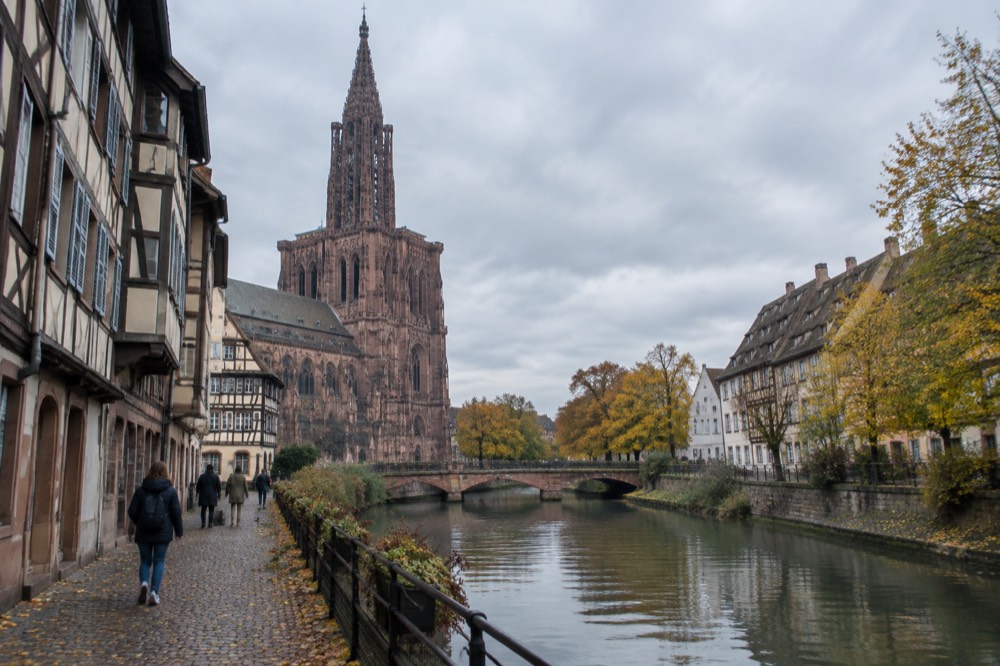 A quiet canal in Strasbourg with trees in autumn colour behind the old buildings